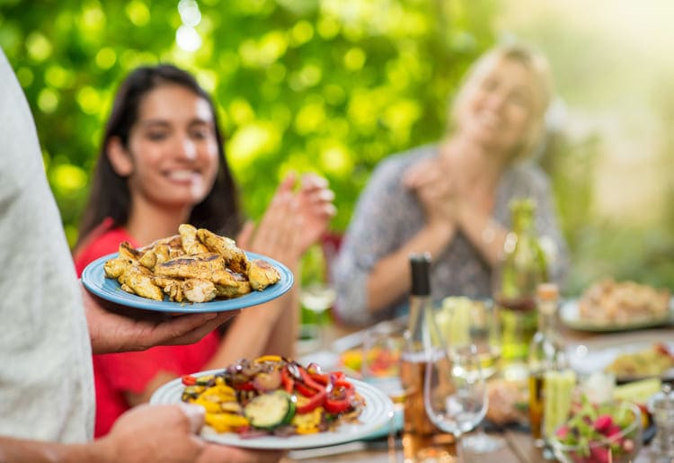 Host serving a high-protein meal with chicken breast and vegetables at a dinner party.