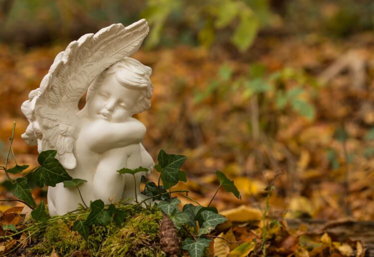 An angel statue sits on the ground in the forest