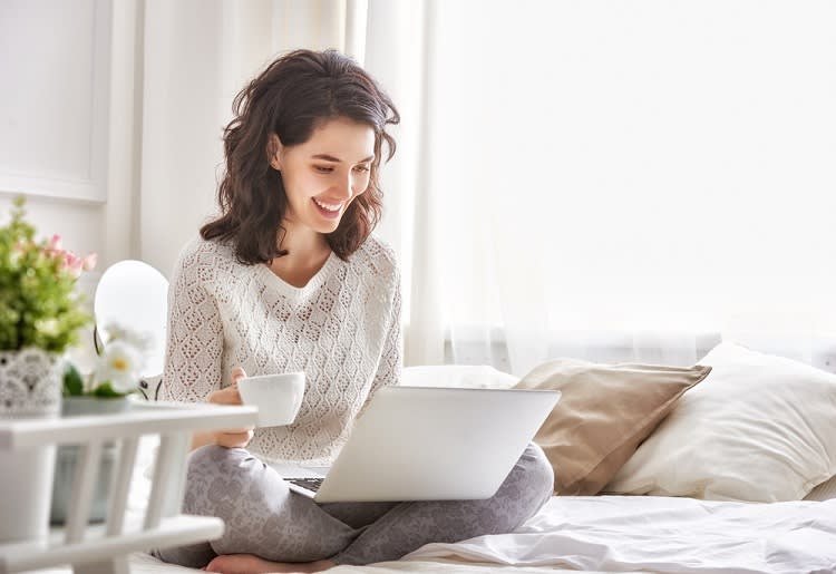 10 Mistakes to Avoid When Buying a Home Warranty in the US Woman using laptop and drinking coffee on bed